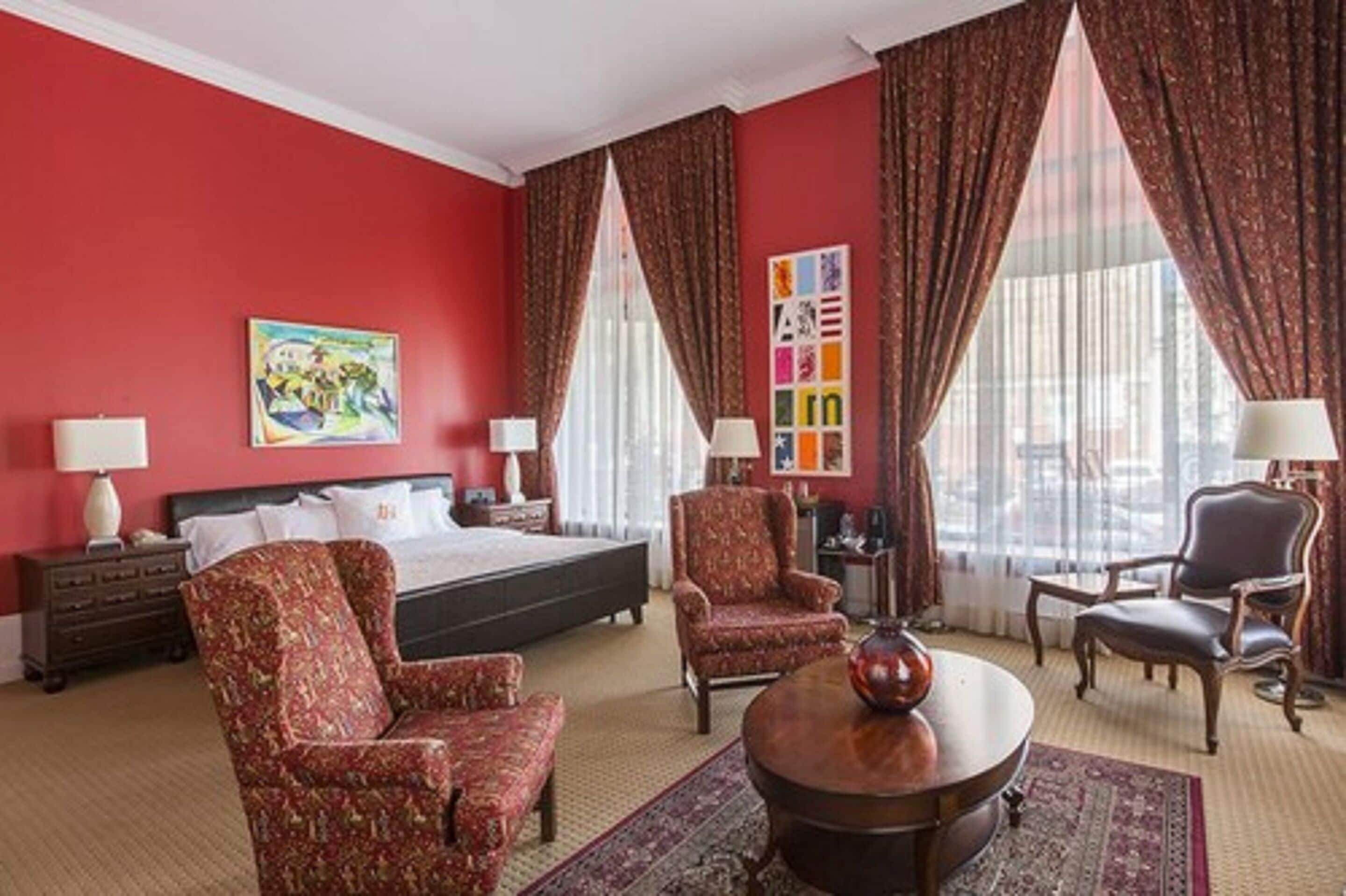 Une chambre d’hôtel avec un grand lit, deux fauteuils, une table basse ronde et un tableau au mur.