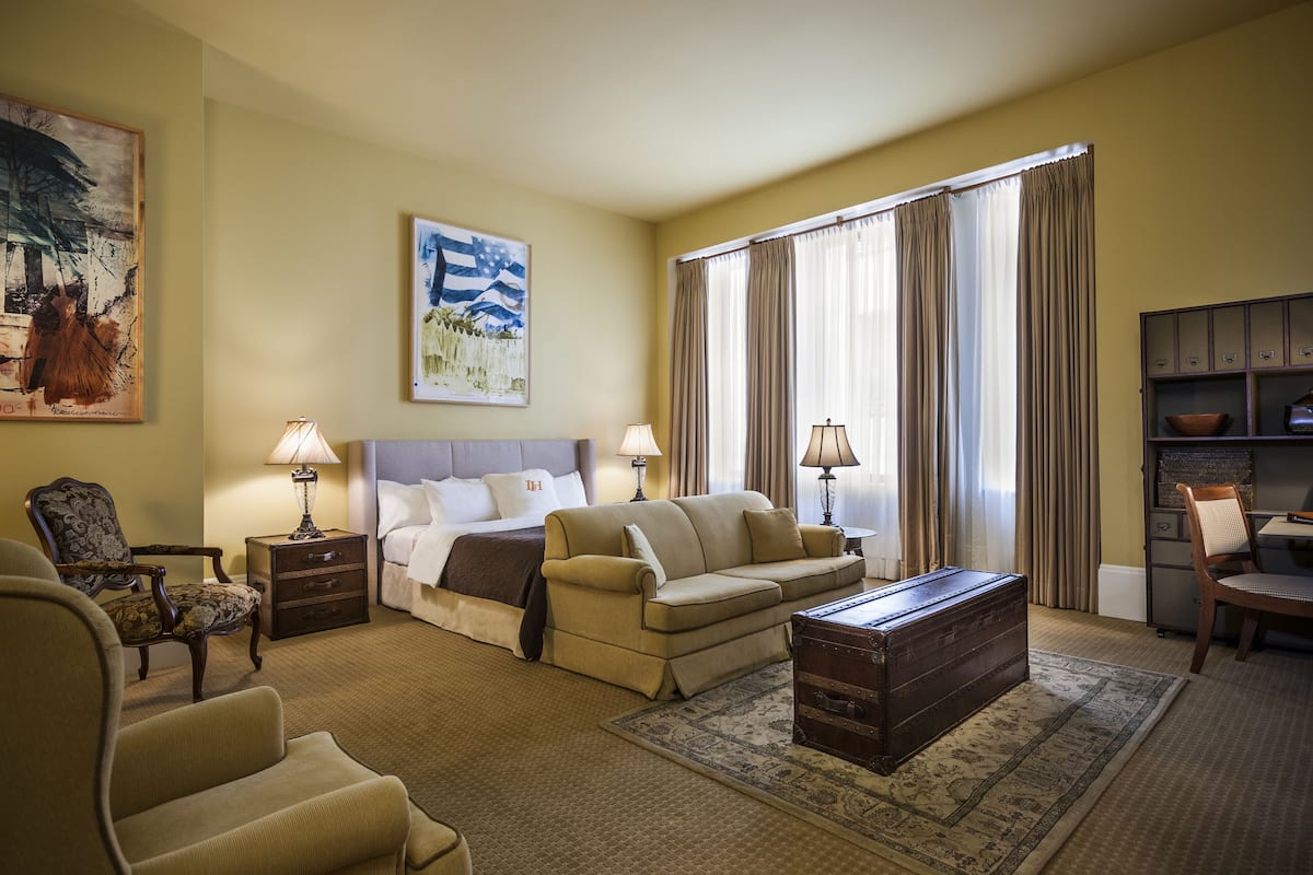 A hotel room with a bed, a sofa, a wooden chest, a desk, and a chair.