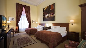 Habitación de hotel con dos camas, un escritorio, una silla, un televisor y un cuadro en la pared.