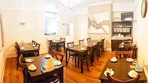 Zona pranzo con diversi tavoli e sedie, un lampadario e angolo cottura con scaffali.
