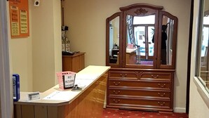Una camera d'albergo con un comò in legno, uno specchio, una tappeto rosso a motivi, una scrivania con un cestino per le chiavi e una bacheca con un cartello.