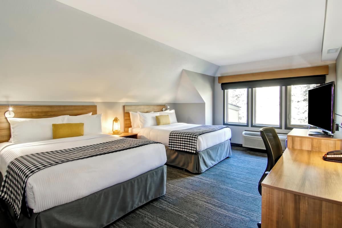 Quarto de hotel com duas camas, uma mesa, uma televisão e uma janela grande.