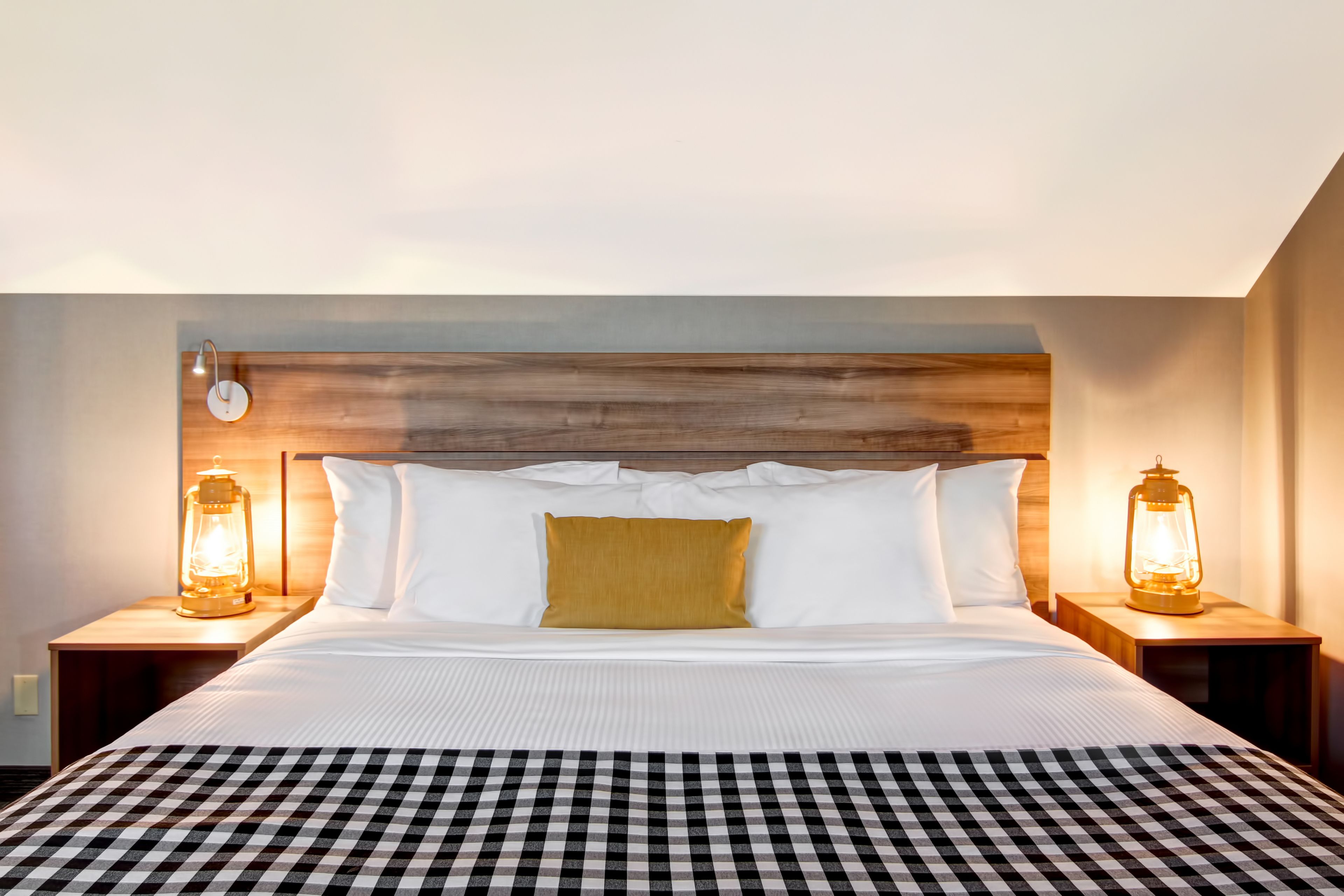 A hotel room with a large bed, two bedside tables with lantern-style lamps, a wooden headboard, and a checkered bedspread.