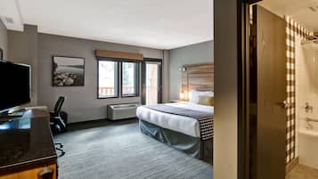 Habitación de hotel con cama, escritorio, televisión, ventana con persianas y baño con pared a cuadros.