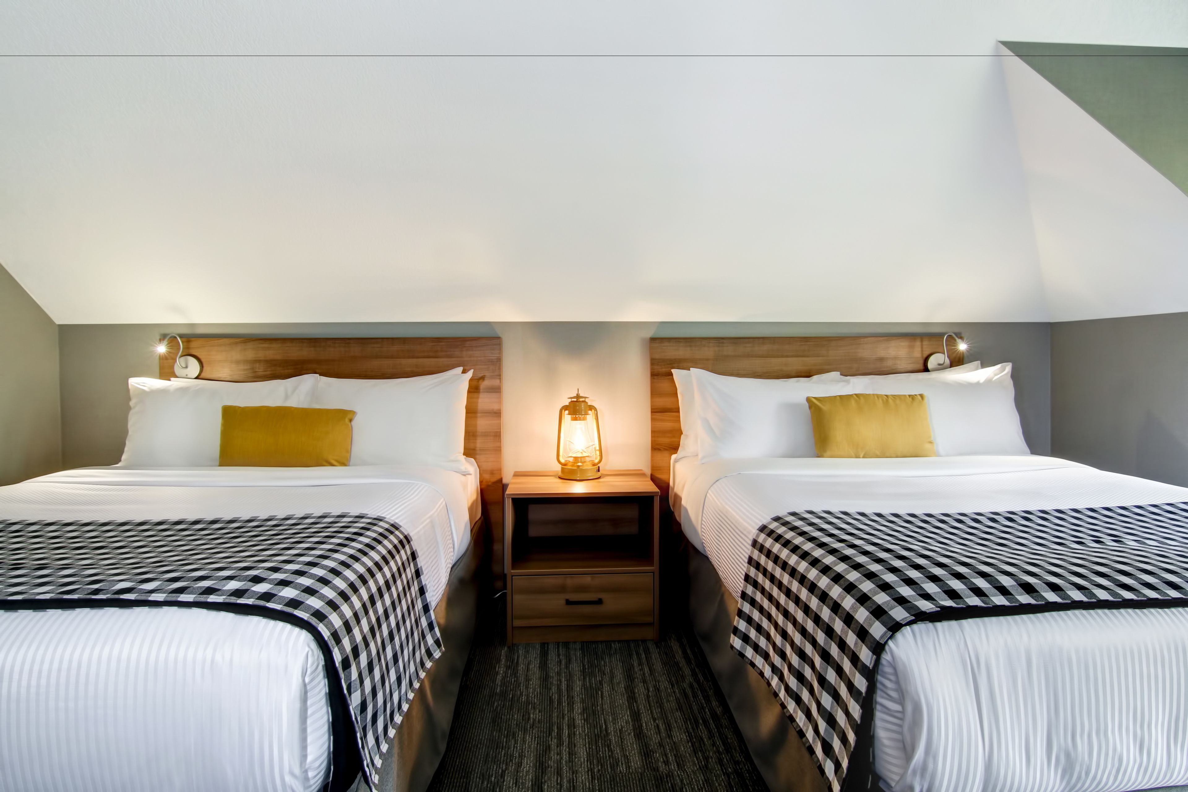 A hotel room with two beds, a nightstand with a lamp, and a wooden headboard.