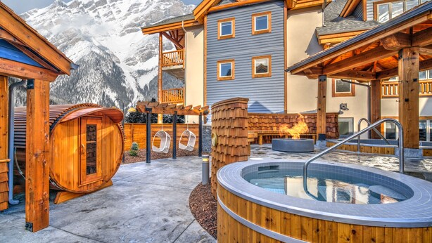 Een houten hut met een hottub, een houten terras en een berg op de achtergrond.