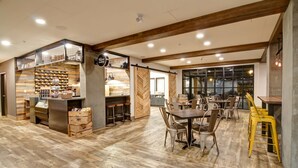 Een ruime restaurantruimte met houten vloeren, een bar en een eetzône met meerdere tafels en stoelen.
