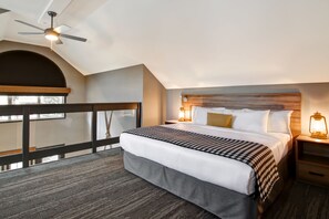 A hotel room with a large bed, a wooden headboard, a nightstand with a lantern, and a balcony with a railing.