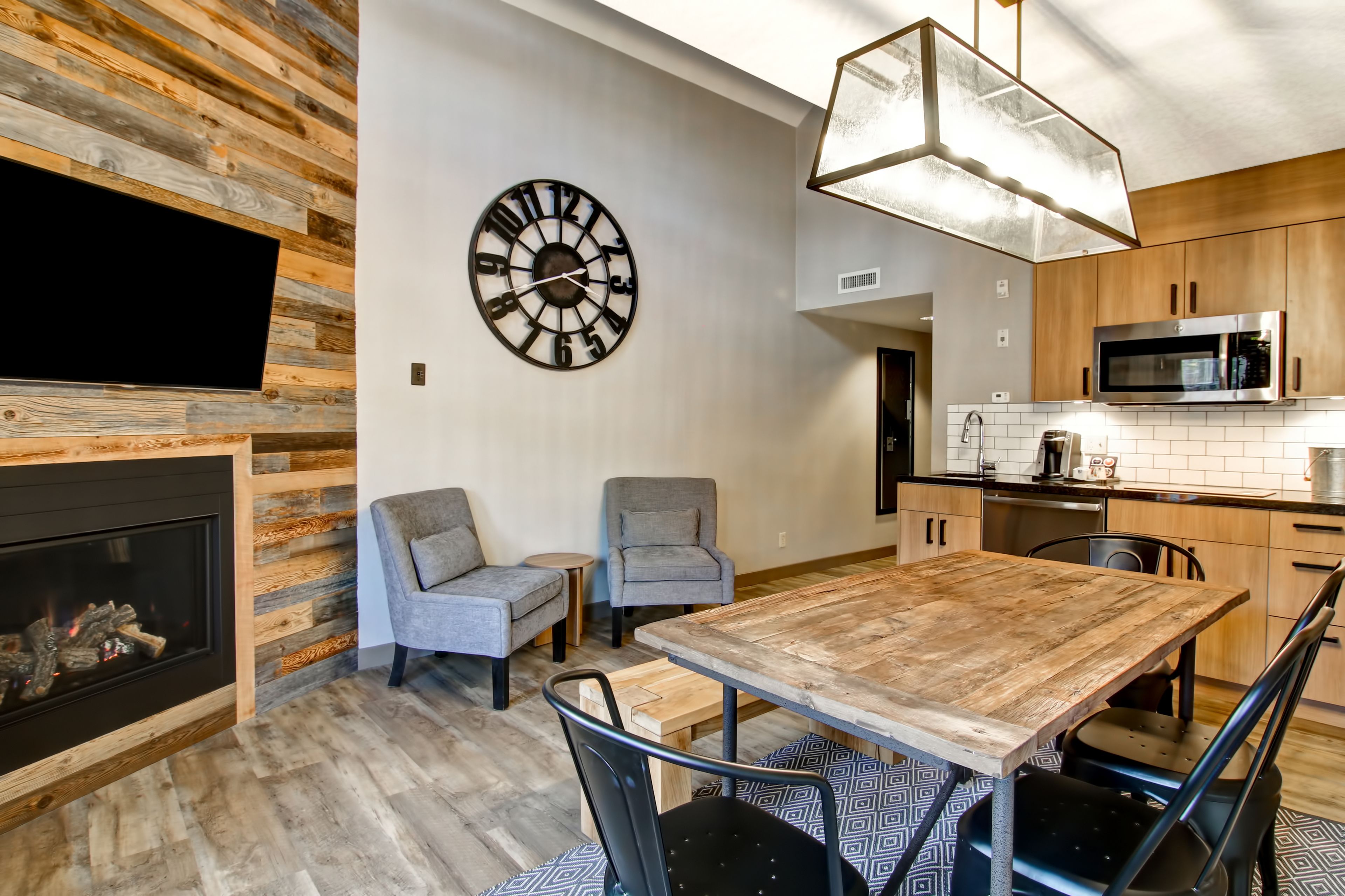 Une cuisine moderne avec un mur en bois, une grande horloge et un coin repas comprenant une table et des chaises en bois.