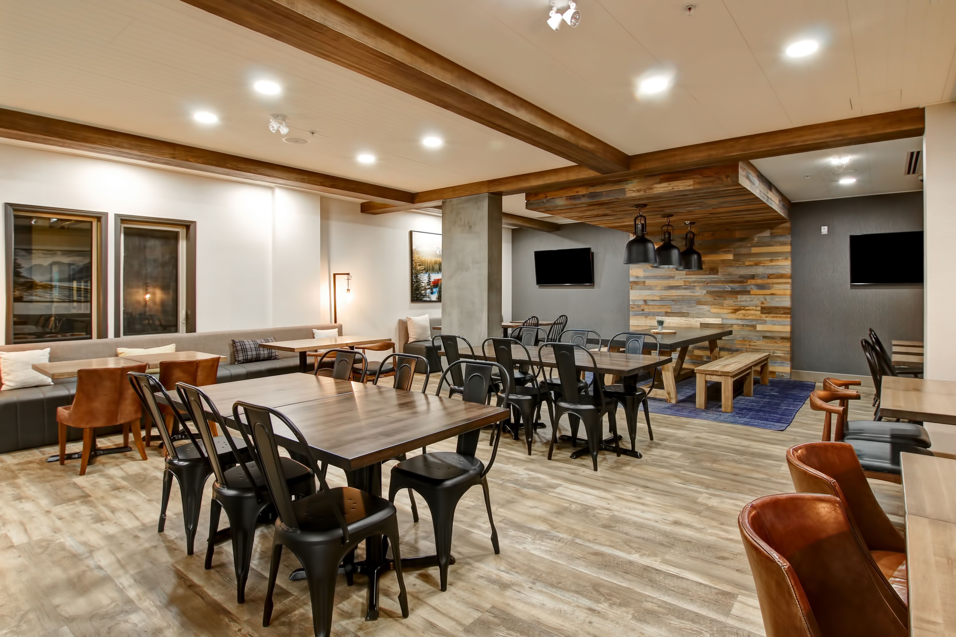 A spacious dining area with multiple tables and chairs, a sofa, and a television mounted on the wall.