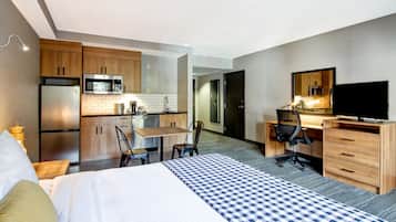 Camera d'albergo con un letto, una scrivania, una sedia, una TV, un forno a microonde, un frigorifero e angolo cottura.