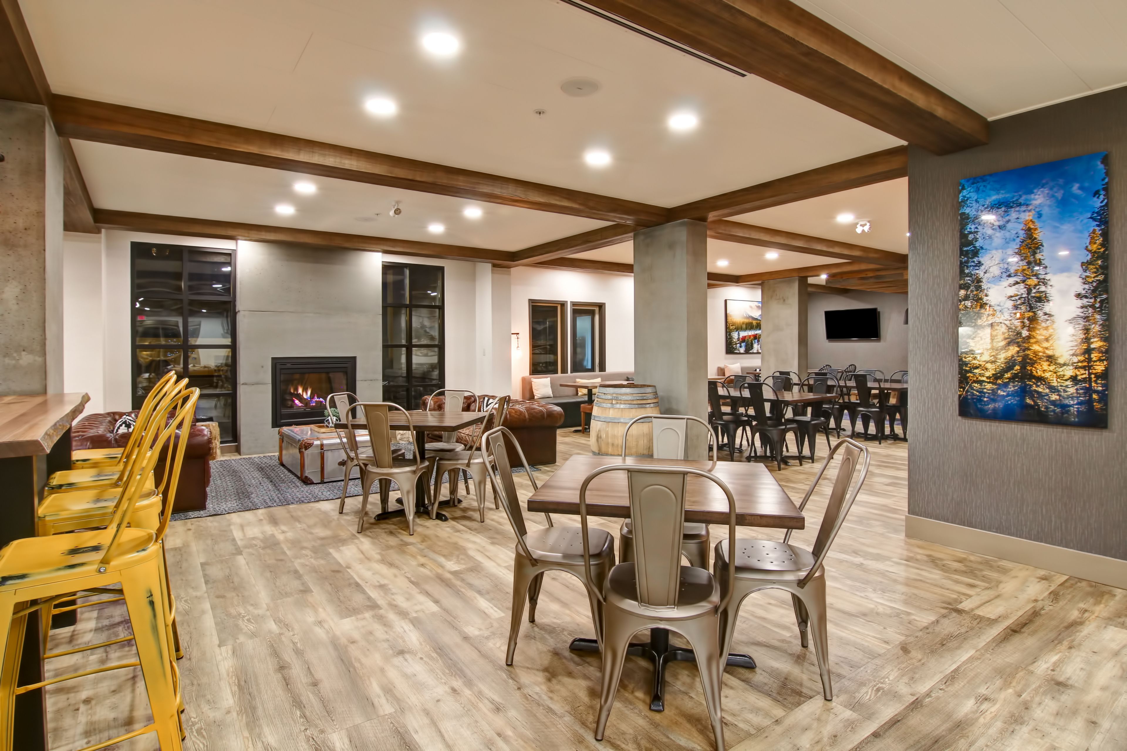 A spacious dining area with wooden tables and chairs, a fireplace, and a large painting on the wall.