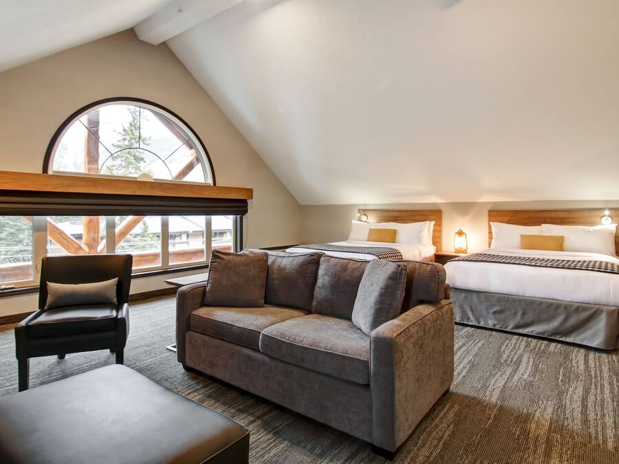 A hotel room with a loft bed, a sofa, a chair, and a large window offering a view of the outdoors.