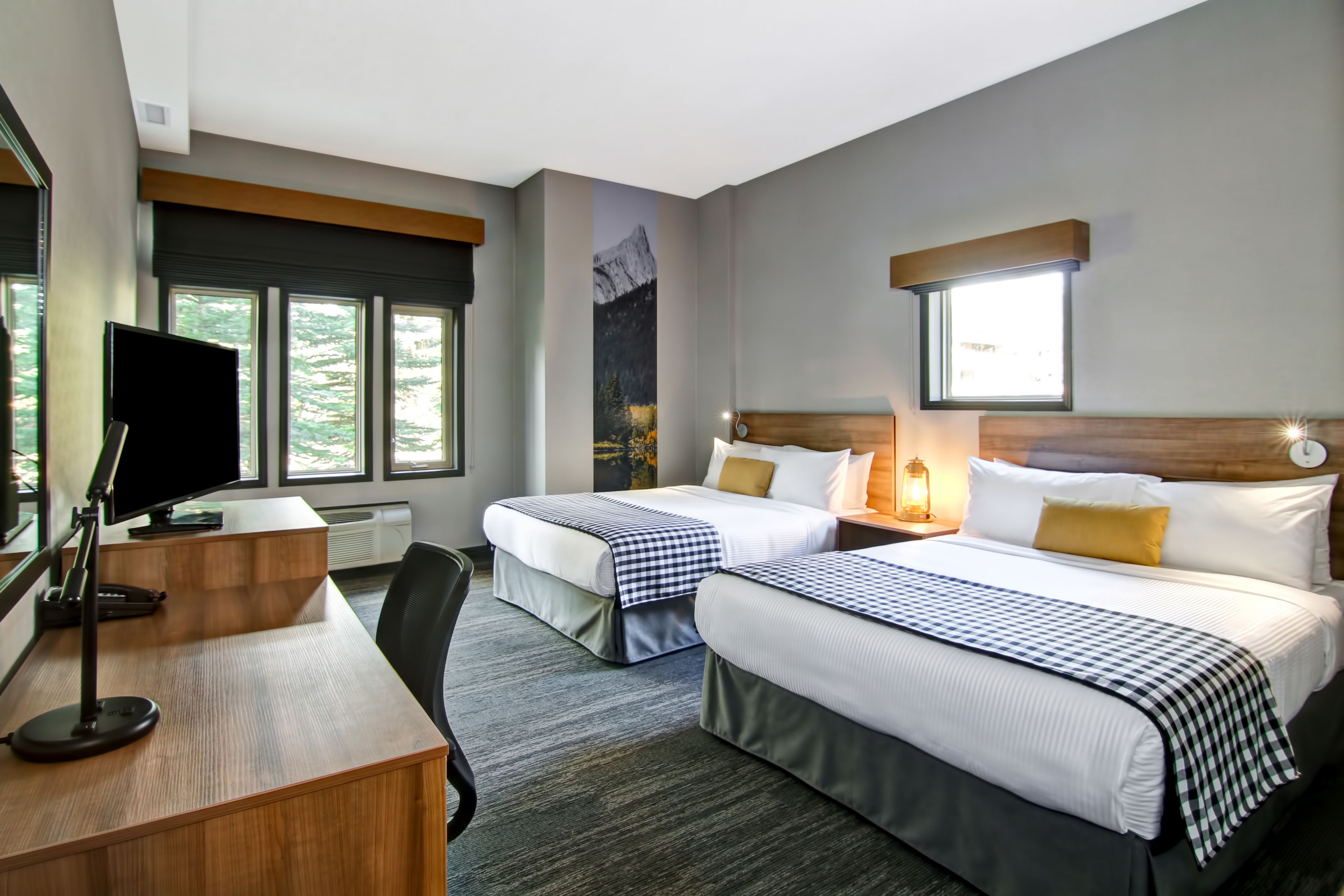 A hotel room with two beds, a desk, a chair, and a TV.