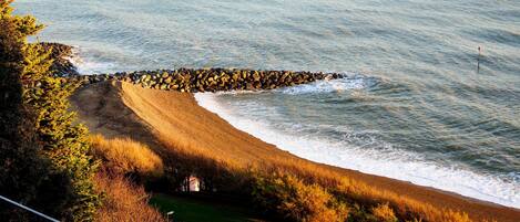 A coastal landscape with a rocky breakwater, a sandy beach, and a grassy area with trees.