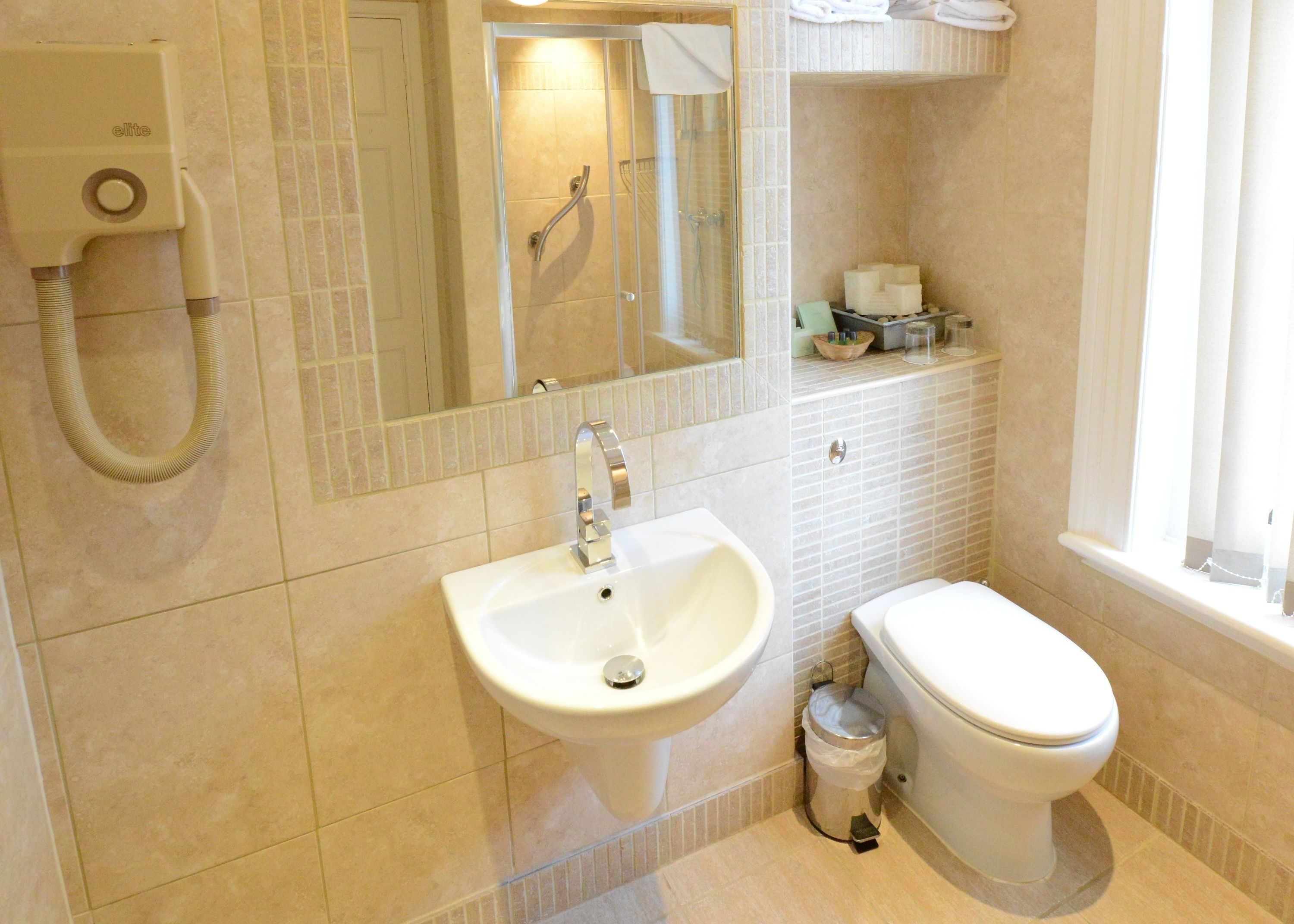A bathroom with a sink, toilet, and shower. There is a towel rack and a trash can.