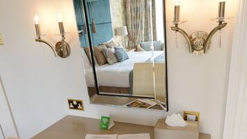 A hotel room with a large mirror, bedside lamps, a bed with pillows, a bedside table with a brochure, and a tissue box.