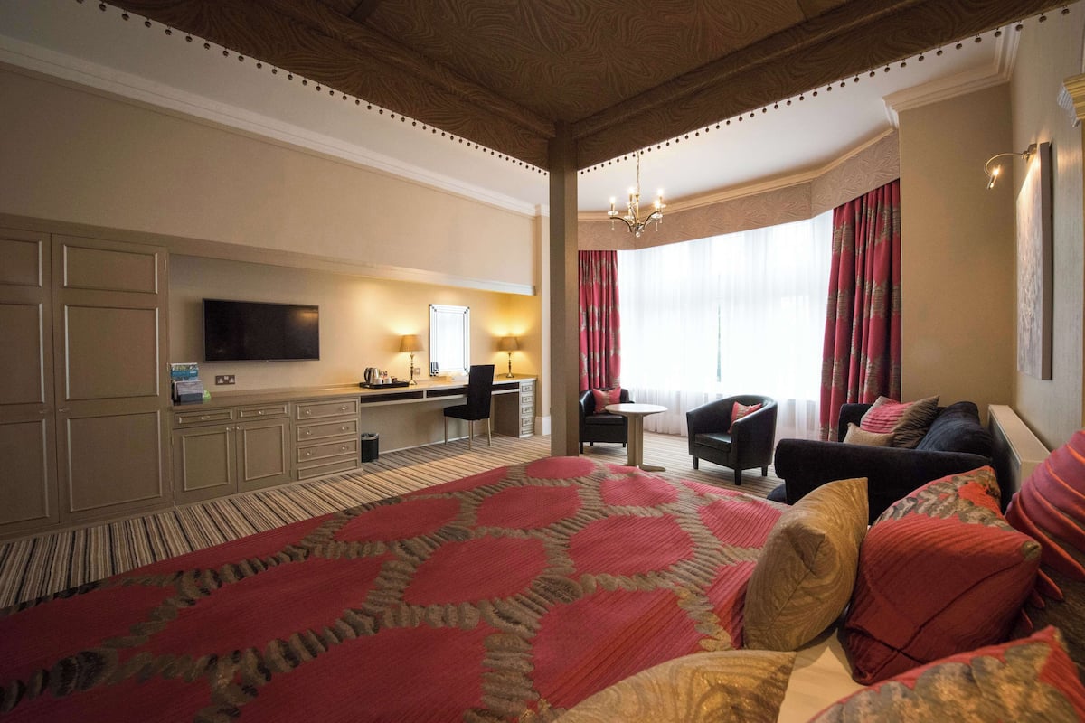 Ein Hotelzimmer mit einem großen Bett, einem Schreibtisch mit Stuhl, einem Fernseher und einem Fenster mit Vorhängen.
