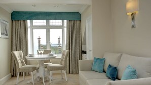 Um quarto com uma mesa de jantar redonda, duas cadeiras, um sofá branco com almofadas azuis e vista para uma torre distante através de grandes janelas.