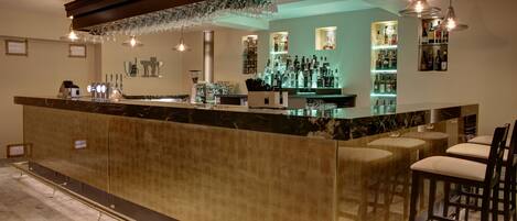 A bar area with a marble countertop, bar stools, and hanging light fixtures.