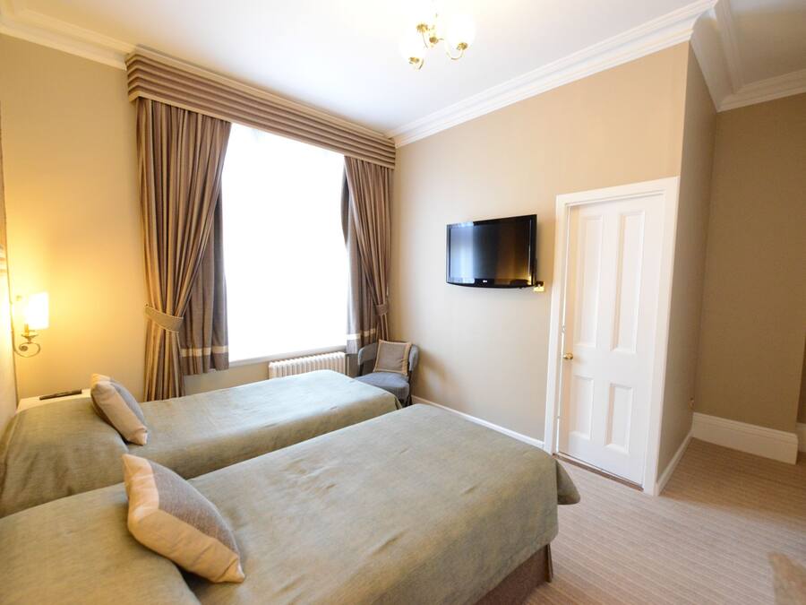 A hotel room with two beds, a television on the wall, a window with curtains, and a door.