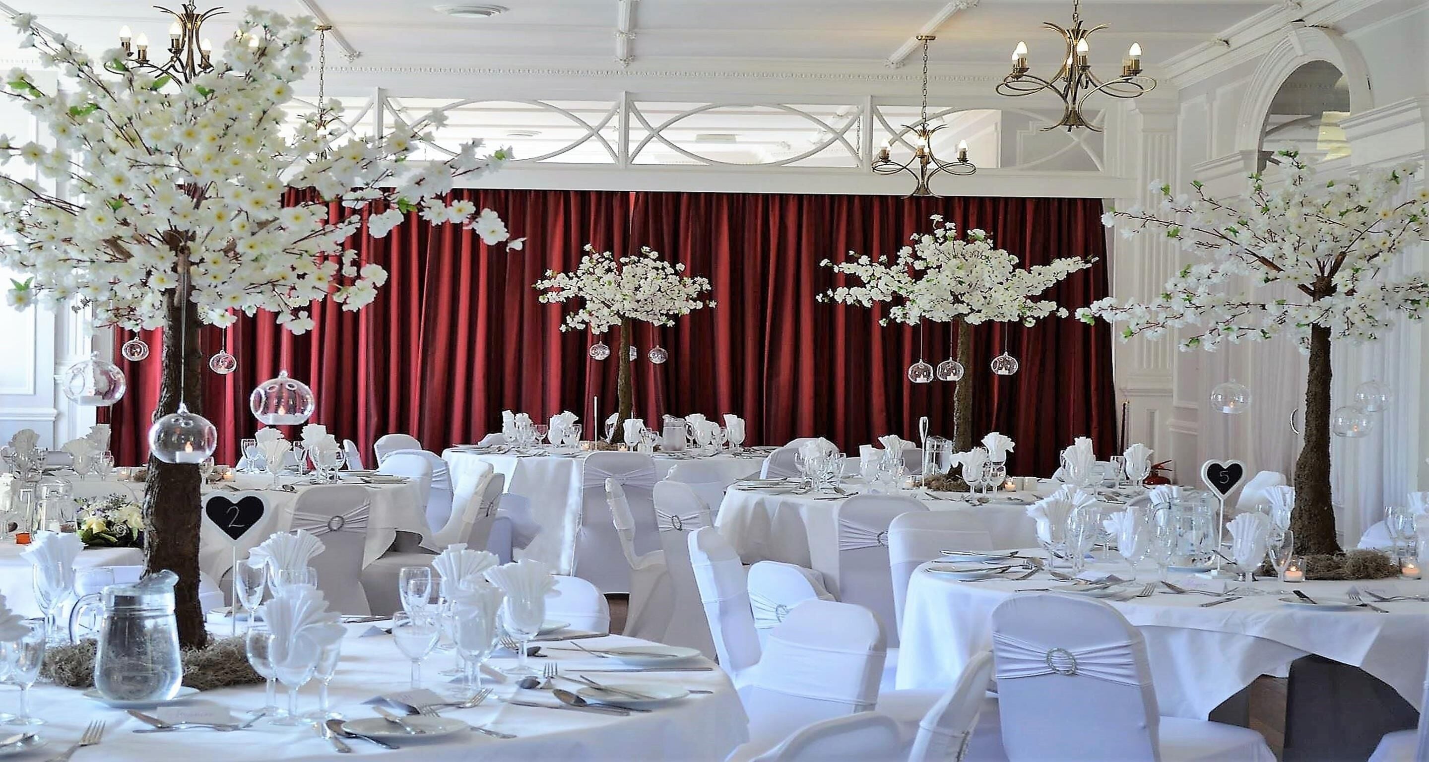 Un salón de banquetes con mesas dispuestas para un evento formal, decorado con flores blancas y elegantes centros de mesa.