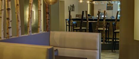 A cozy dining area with a booth seating arrangement, a bar in the background, and pendant lighting.