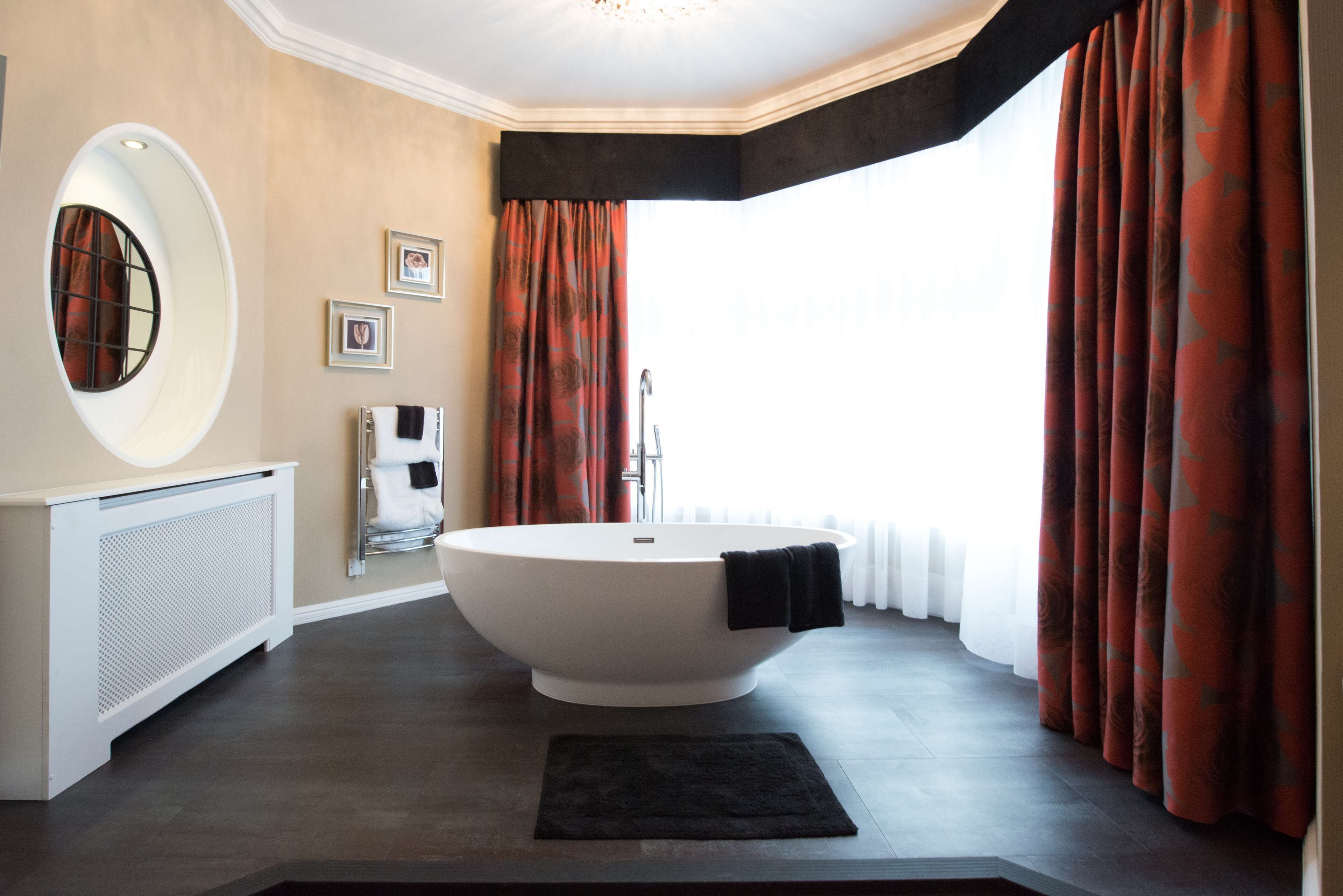 Ein modernes Badezimmer mit einer freistehenden Badewanne, einem großen Spiegel und einem Fenster mit Vorhängen.