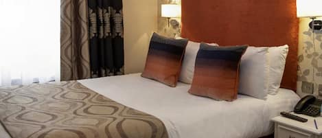 Una habitación de hotel con una cama, dos almohadas, una mesita de noche con un teléfono y una lámpara.
