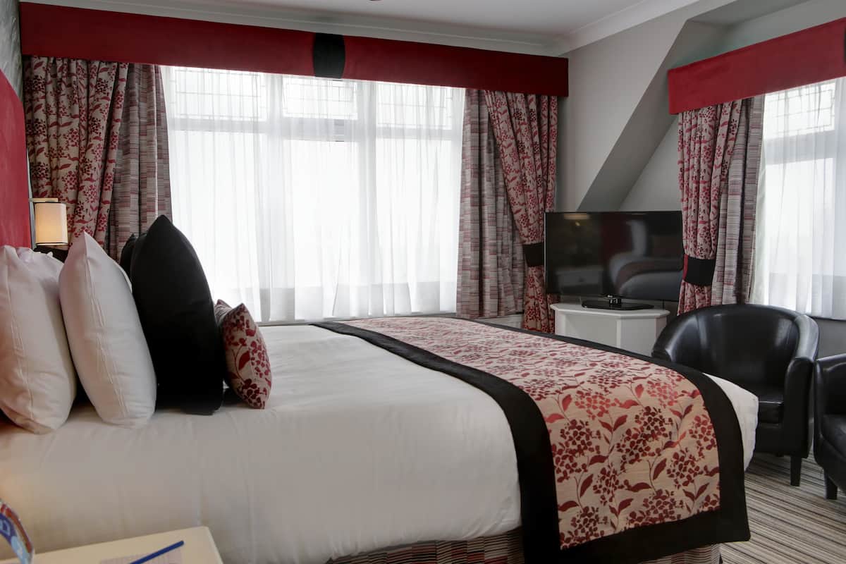 Ein Hotelzimmer mit einem großen Bett, einem Schreibtisch mit Stuhl, einem Fernseher und Vorhängen.