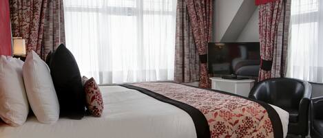 A hotel room with a large bed, a desk with a chair, a TV, and curtains.
