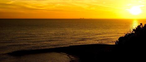 Un atardecer sobre un mar tranquilo con una costa rocosa.