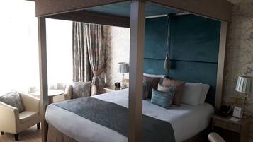 Ein Bett mit Himmelbett, ein Nachttisch mit Lampe und ein Sessel.