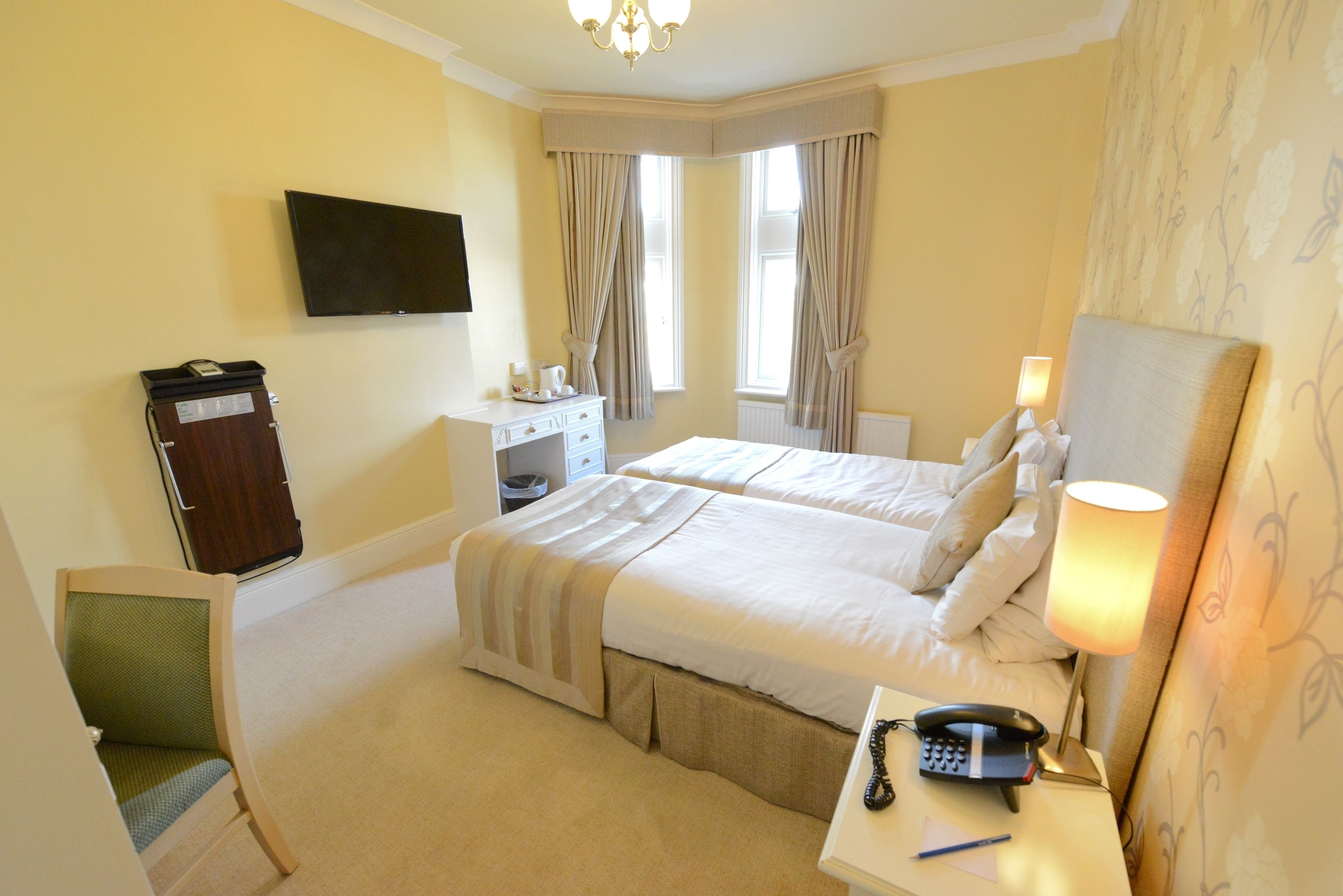 A hotel room with two beds, a desk with a lamp, a telephone, and a television on the wall.