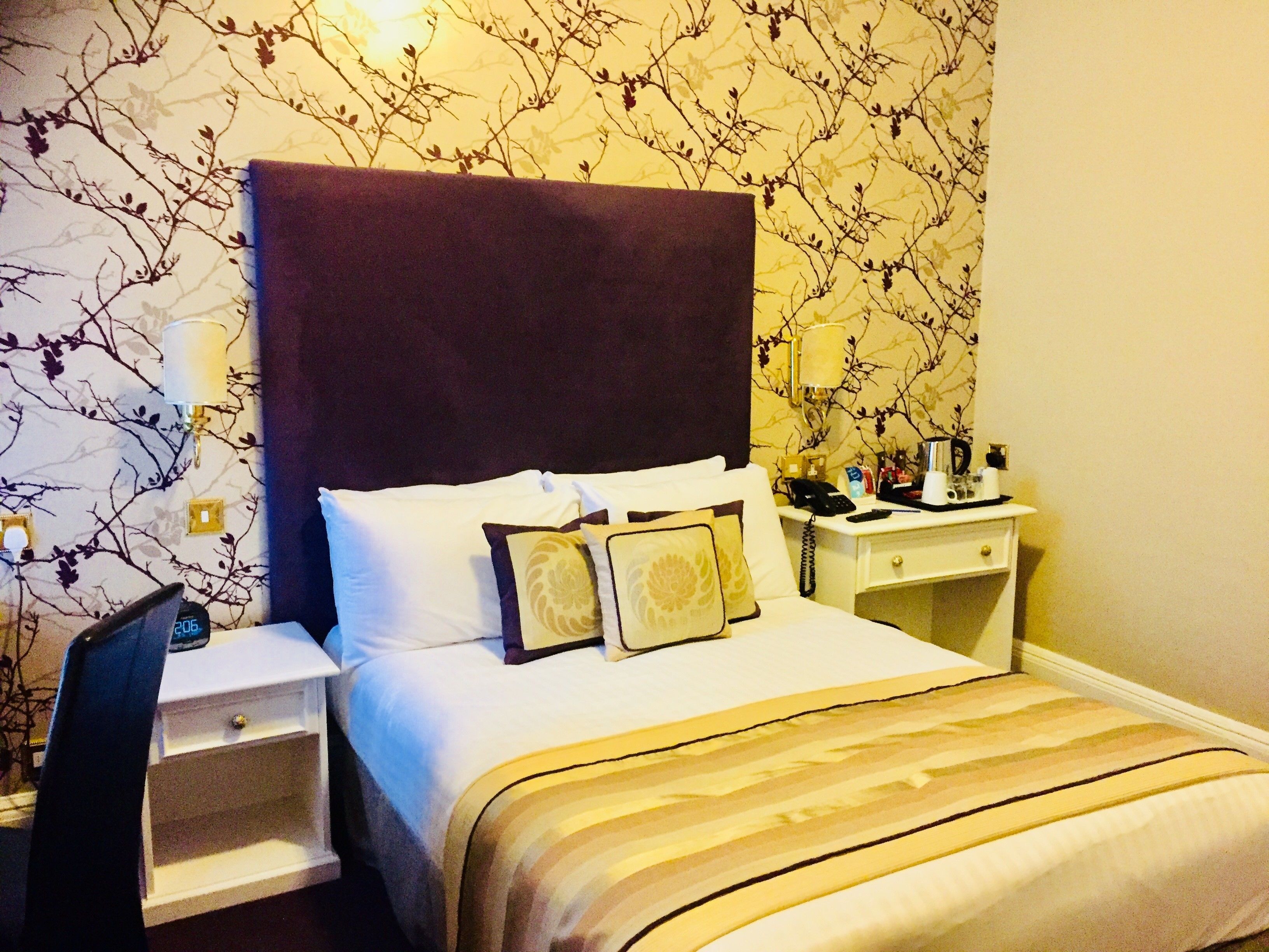 A hotel room with a large bed, a nightstand, a desk, and a chair.