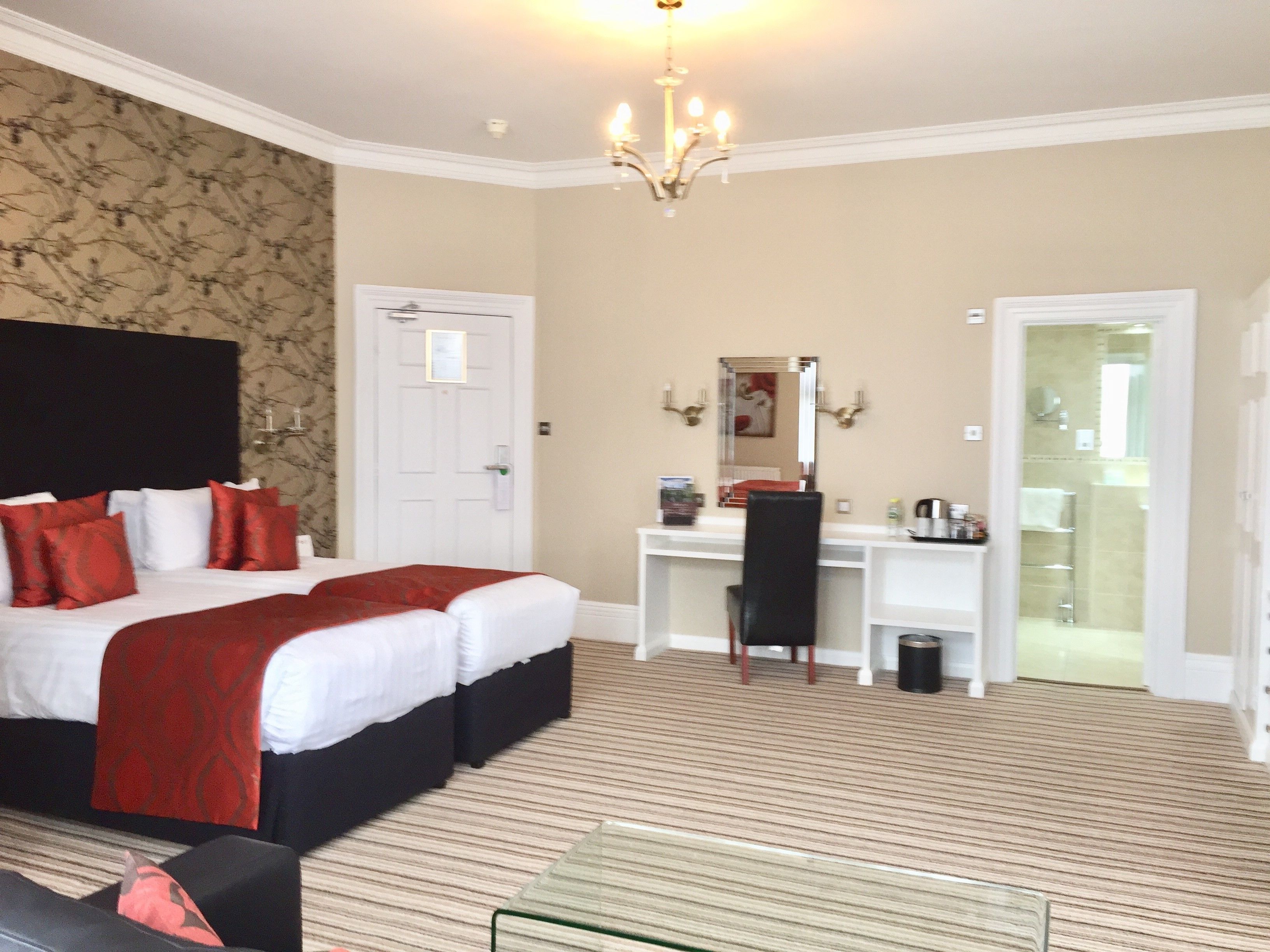 A hotel room with a large bed, a desk, a chair, a mirror, and a shower area.