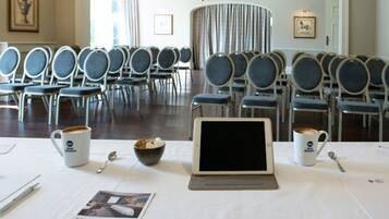 Un salón de conferencias con filas de sillas, una computadora portátil sobre una mesa y dos tazas de café con cucharas.