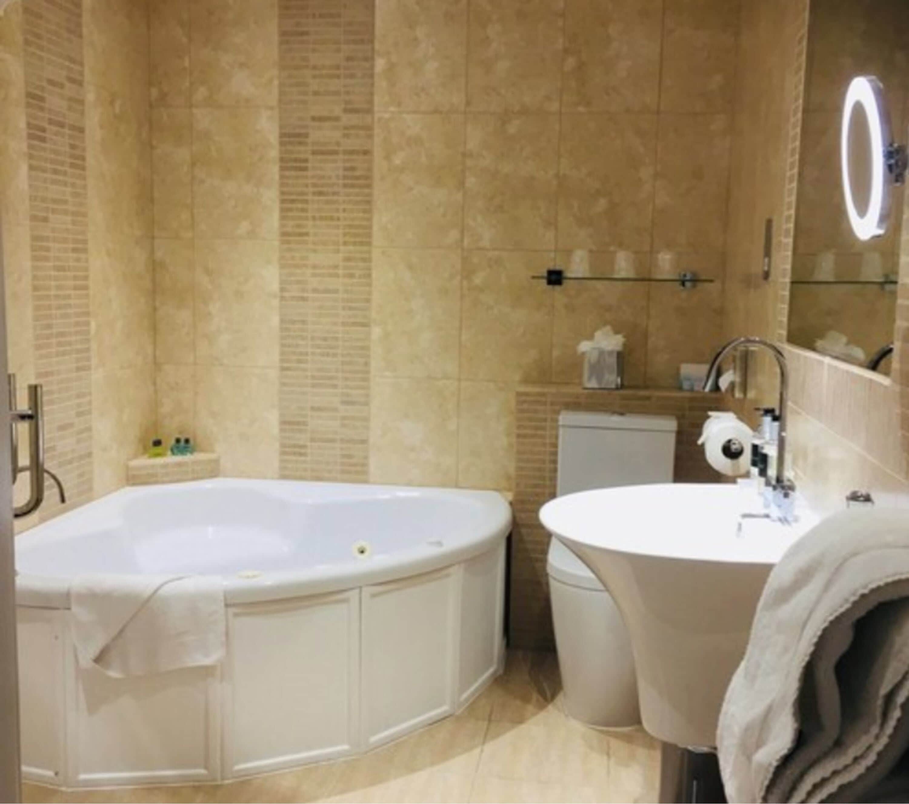 A bathroom with a freestanding bathtub, a sink, and a mirror with a light.