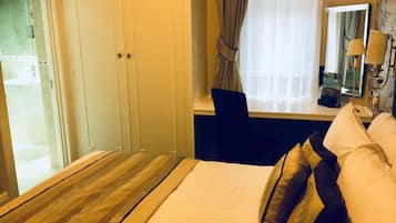 Una habitación de hotel con cama, escritorio, silla, ventana con cortinas y baño visible a través de una puerta abierta.