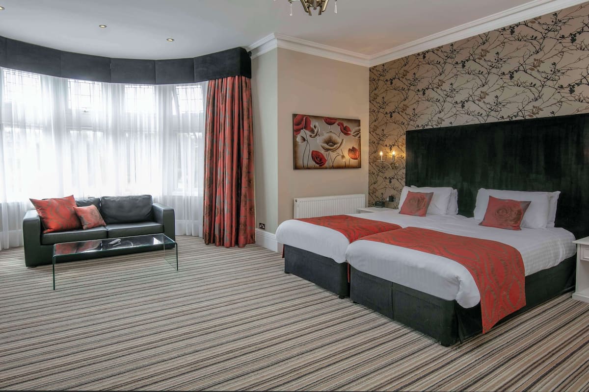 Ein Hotelzimmer mit Doppelbett, einer Couch, einem Couchtisch und einem großen Fenster mit Vorhängen.