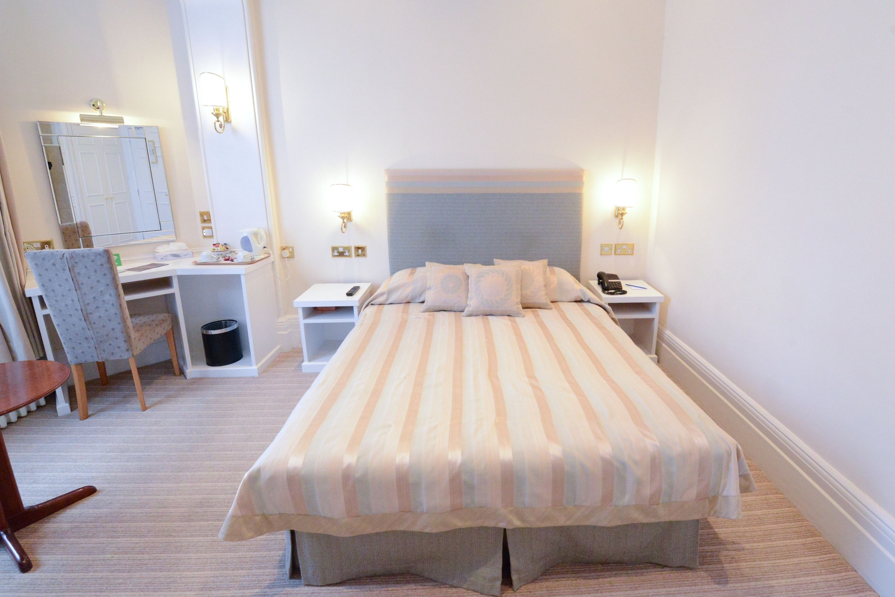 Ein ordentlich eingerichtetes Schlafzimmer mit Bett, Nachttischen, einem Sessel, einem Schreibtisch und einem Spiegel.