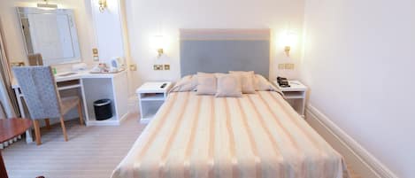 A neatly arranged bedroom with a bed, bedside tables, a chair, a desk, and a mirror.