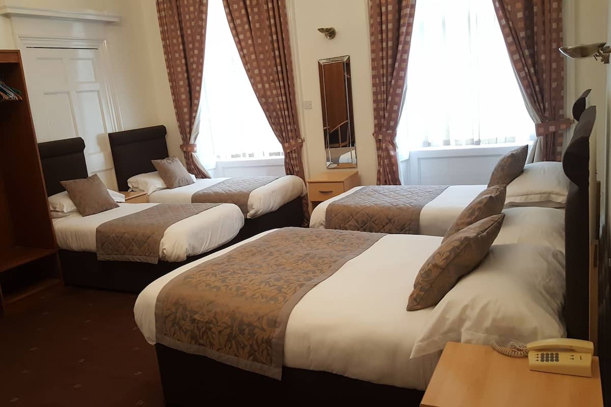 A hotel room with two beds, a wardrobe, a desk, a telephone, and a window with curtains.