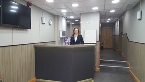 Un'area reception con una scrivania, una sveglia e un televisore a parete.