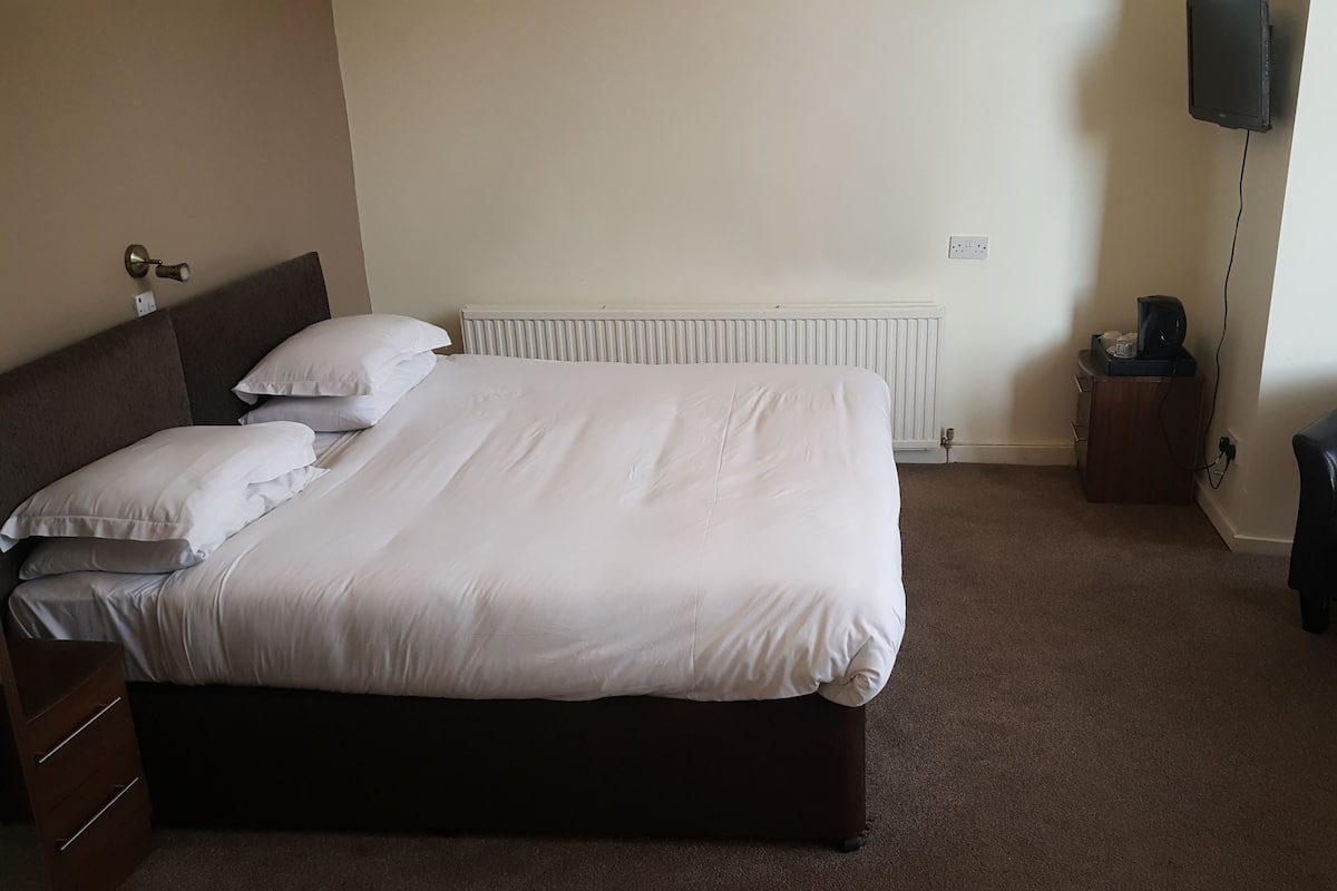 A neatly made bed with white linens, a dark headboard, and a wooden dresser with drawers.