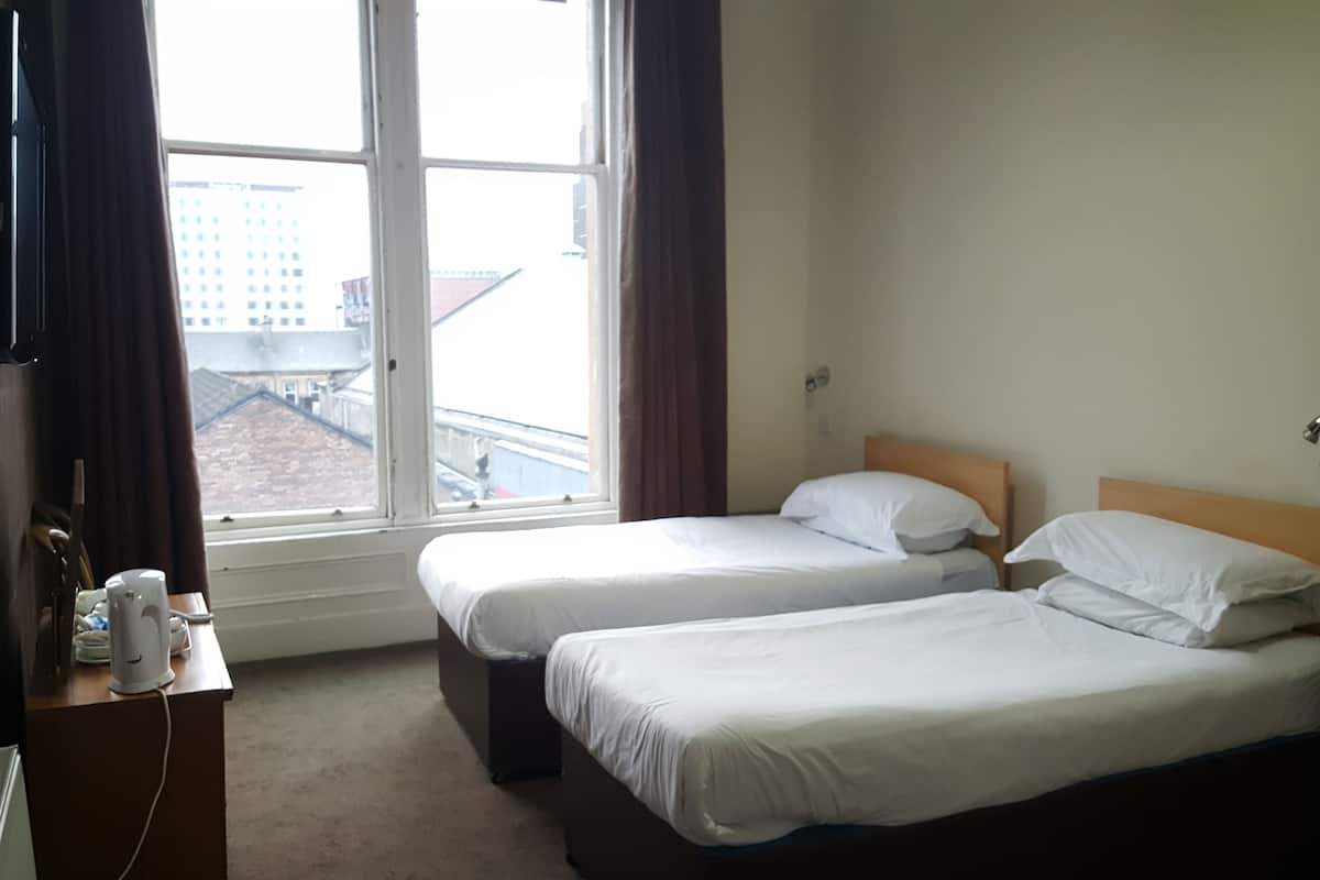 A hotel room with two single beds, a desk with a telephone, and a window with curtains.