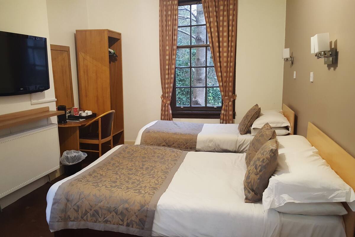 A hotel room with two beds, a TV, a desk, and a window with curtains.