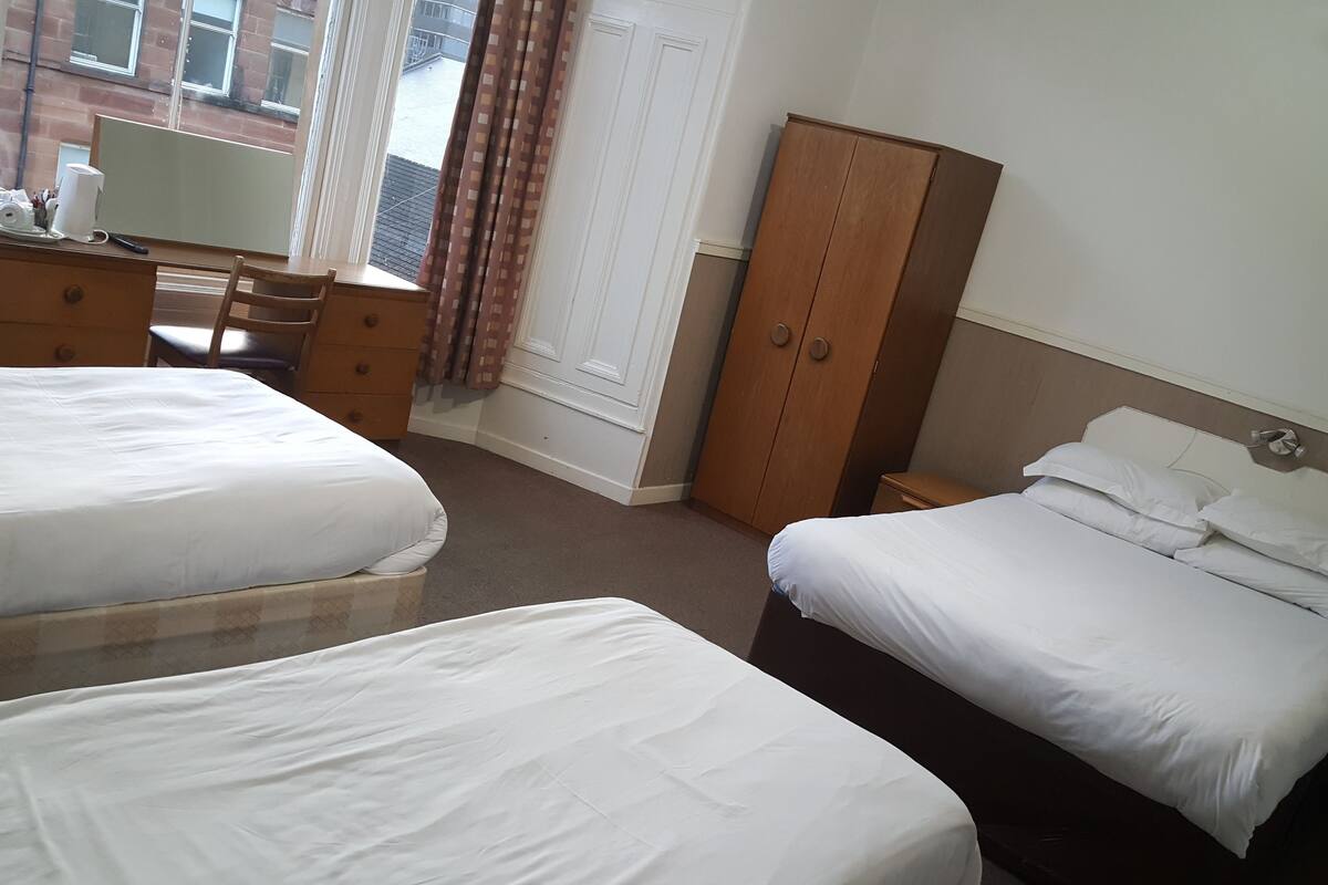 A hotel room with two beds, a desk with a chair, a wardrobe, and a window with curtains.