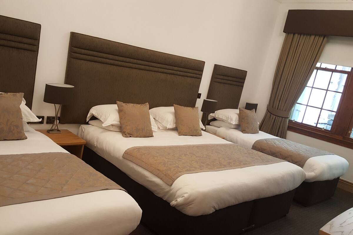 A hotel room with three beds, each with a headboard, bedside tables, and lamps.