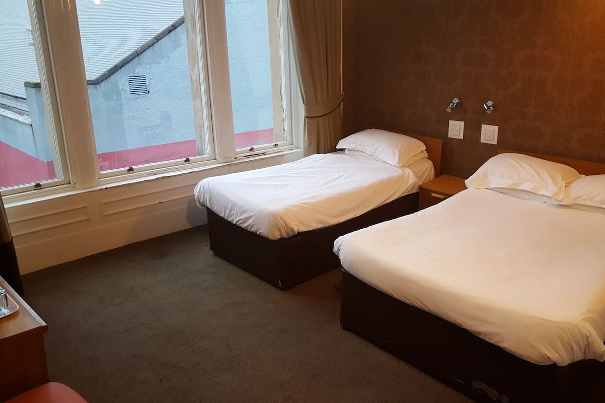 A hotel room with two single beds, a small bedside table, a nightstand, and a window with curtains.